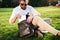 Serious bearded man sitting on grass outdoors getting tablet computer