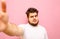 Serious bearded overweight guy in a white T-shirt stands on a pink background and takes a selfie . Charismatic fat man takes a