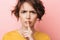 Serious beautiful woman posing  over pink wall background showing silence gesture