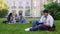 Serious biracial male student sitting on grass and writing essay, doing homework