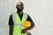 Serious black man in reflective vest and eyeglasses holding hardhat by his waist