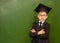 Serious boy in graduation cap standing near green chalkboard
