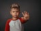 Serious boy shows his hand to the camera. Gesture asking to stop. Boy frowns in studio. High quality photo