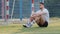 Serious, brooding Middle Eastern footballer sitting on grass of soccer field against goal, resting after game or