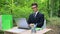 Serious businessman in suit working on laptop at office desk in forest fresh air