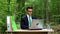 Serious businessman working on laptop at office desk in forest, air conditioning