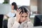 Serious busy beautiful Asian woman officer has headache and puts head in hand while working at office desk with working colleagues
