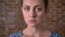 Serious calm close-up face of brunette caucasian woman who is standing ner brick wall inside