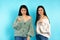 Serious caucasian twin girls show their fist and look at the camera. Blue background.