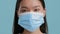 Serious Chinese Lady Wearing Protective Face Mask On Blue Background