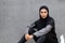 Serious confident young islamic lady in sportswear and hijab with bottle of water sits on floor