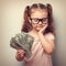 Serious cute kid in glasses looking on dollars in hand and think