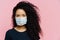 Serious dark skinned young woman being on self isolation at home, wears protective medical mask, being on quarantine at home,