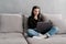 Serious determined young businesswoman or freelancer in casual clothes sitting on sofa and looking at laptop screen