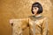 Serious Egyptian woman like Cleopatra with thumbs down gesture, on golden background