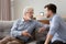 Serious elderly father and grownup son sitting on couch talking