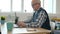 Serious elderly man using computer at home typing sitting at desk indoors
