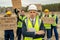 Serious employer in hardhat standing in front of protestants