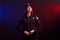 Serious female police officer is posing for the camera against a black background with red and blue backlighting.