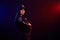 Serious female police officer is posing for the camera against a black background with red and blue backlighting.