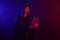 Serious female police officer is posing for the camera against a black background with red and blue backlighting.