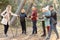 Serious female sports trainer with group of people talking, explaining posture for Nordic walking with sticks in forest