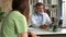 Serious focused aged physician in medical coat sitting at table, consulting female patient about illness or surgery