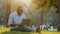 Serious focused senior black person sitting on grass in park using laptop, African American mature male works online