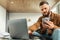 Serious Freelancer Man Using Phone And Laptop At Home