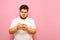 Serious funny overweight man uses smartphone on pink background. Fat guy in white t-shirt uses internet on smartphone, isolated.