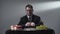 Serious gentleman in the suit sitting at the small table in front of peace of meat, grapes, apples, red wine and candles