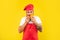 Serious guy in cooking apron and toque smelling tomatoes yellow background, chef