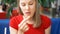 Serious hungry young woman in red t-shirt sitting in cafe eating french fries dipping it in sauce