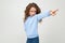 Serious lady teen girl in casual blue hoodie points a finger to the side on a light gray studio background