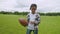 Serious little black boy holding american football ball on field