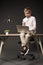 serious little boy holding eyeglasses and using laptop while sitting on table with plant and lamp on grey