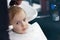 Serious and little scared cute blond baby boy with blue eyes in a barber shop having washing head by hairdresser.