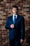 Serious male lawyer businessman in strict business suit and tie standing in the interior against the brown brick wall background