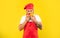 Serious man in cooking apron and toque smelling tomatoes with closed eyes yellow background, cook