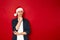 serious man in thoughtful pose holds his hand under his chin in Christmas Santa Claus hat isolated on red background