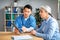 Serious middle aged asian man doctor showing tablet to retired european woman patient in clinic