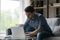 Serious millennial man using laptop, typing, sitting on couch