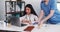 Serious multiethnic female healthcare professional talks to remote patient on laptop webcam, nurse brings vaccine tray.