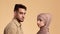 Serious Muslim Couple Turning Head Looking At Camera, Beige Background