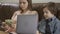 Serious older sister and younger little brother sitting on the leather sofa. The boy holding laptop, the girl counting