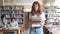 Serious redhead lady walking in library with bunch of books looking around