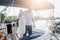 Serious sailor stands on his yacht and looks down. He holds rope with big plastic bottle. Young man is calm and peaceful