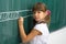 Serious schoolgirl standing at blackboard