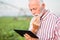 Serious senior agronomist or farmer contemplating while using a tablet in soybean field. Irrigation system blurred in background