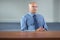 Serious senior businessman sits behind empty desk